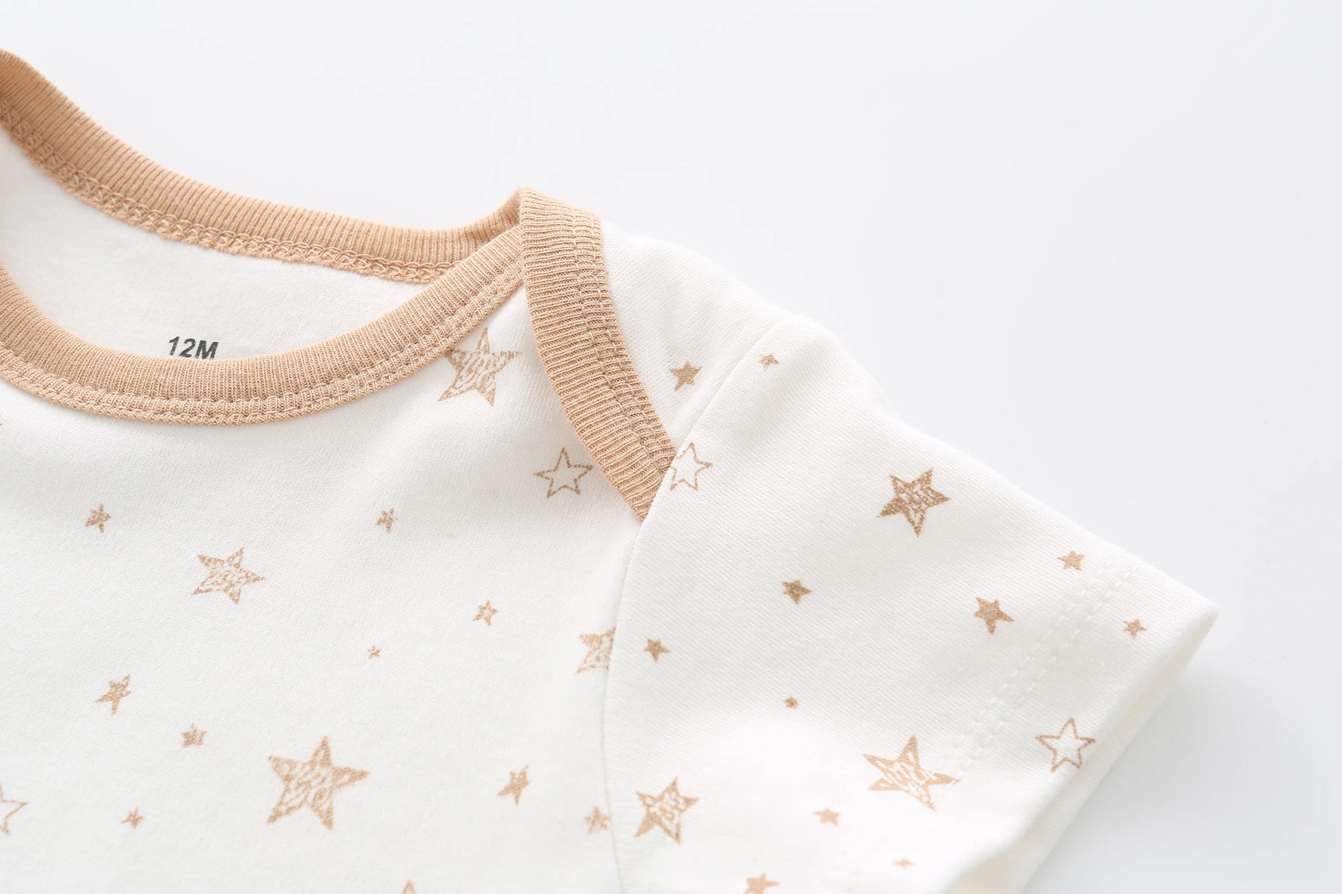 Gros plan sur une combinaison bébé blanche avec bordure marron et motifs étoiles du Lot de 5 Bodys Bébé | Collection Coton Agréables & conforts par BABY PREMA. L'étiquette à l'intérieur indique la taille 12 mois.
