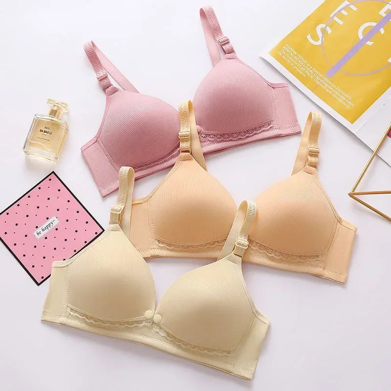 Phrase avec le produit remplacé : Une gamme de soutiens-gorge Elégant Soutien d'Allaitement de BABY PREMA soigneusement disposés dans une composition à plat aux côtés d'un flacon de parfum et d'objets de décoration, dégageant une ambiance poids léger.