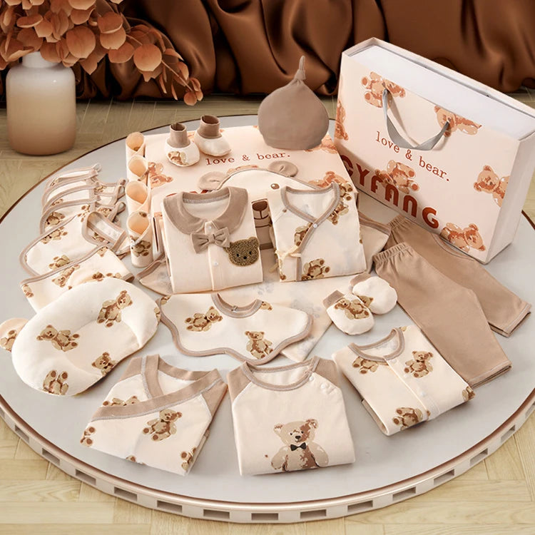 Le Coffret Naissance Coton | Nouveau-nés Douceur Assurée de BABY PREMA, un ensemble complet de vêtements et d'accessoires pour bébé aux motifs d'ours, est présenté sur une table ronde. Ce kit comprend de 20 à 26 articles essentiels tels que des vêtements, des bavoirs, des mitaines, des chapeaux et est accompagné d'une boîte cadeau étiquetée « love & bear », le tout confectionné en coton doux et respirant.