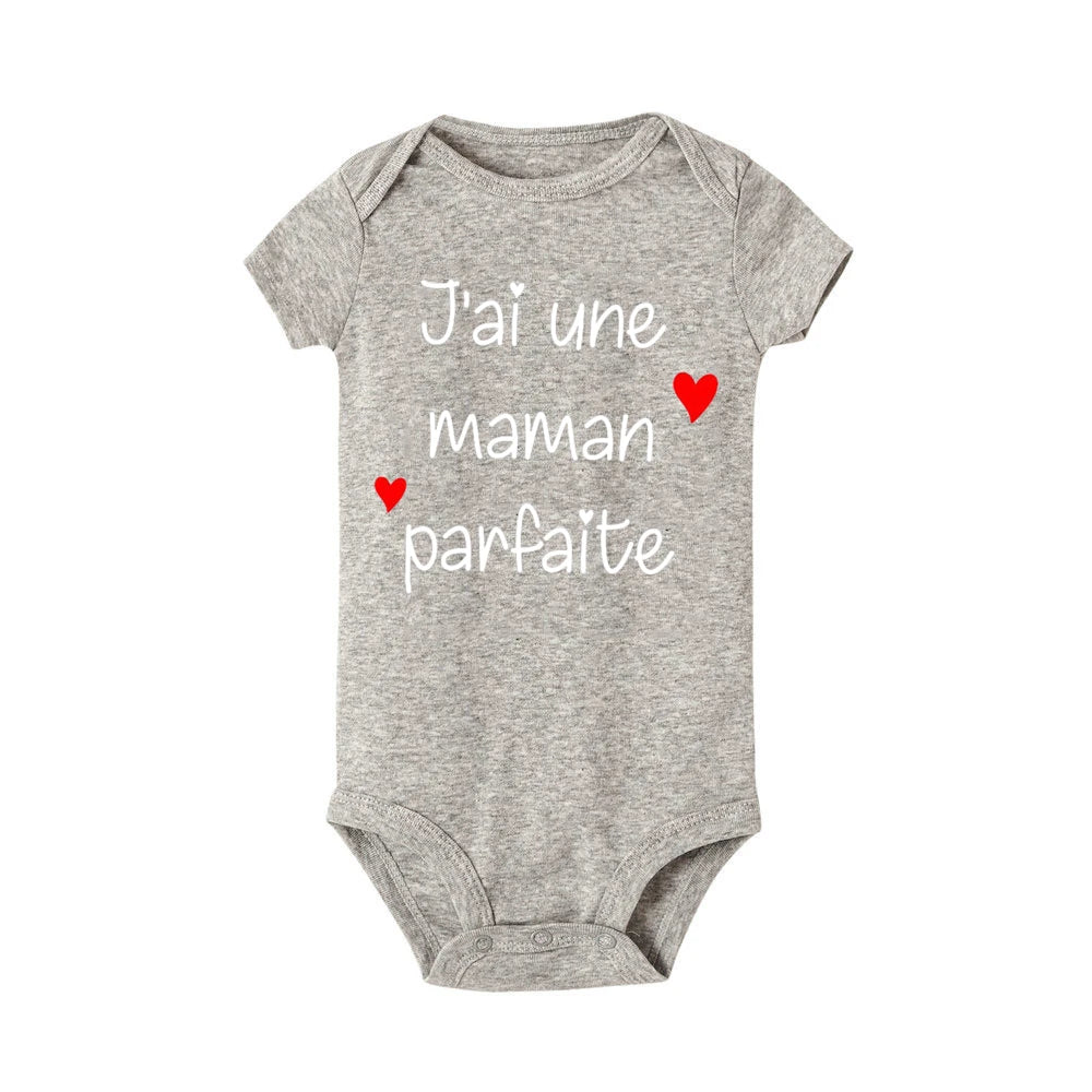 Combinaison bébé grise avec manches courtes et texte français « J'ai une maman parfaite » écrit en blanc, rehaussé de deux petits cœurs rouges — un ajout charmant à toute garde-robe enfant. Il s'agit du Body Bébé Coton Imprimé Préma de BABY-PREMA.