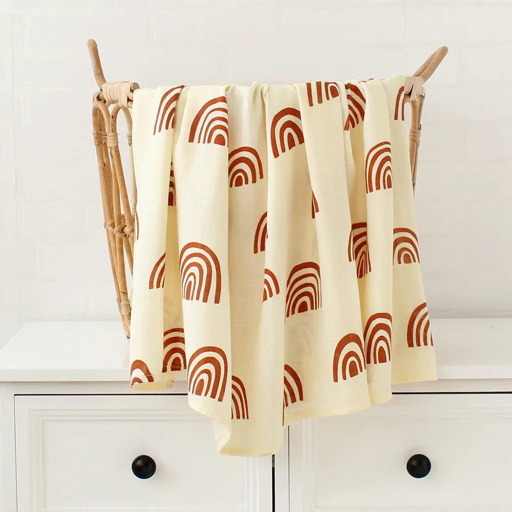 Un linge beige à motif de demi-cercles rouges drapé sur un étendoir en bois dans une pièce au meuble blanc, parfait pour envelopper bébé après le dodo, Lange Bébé en Bambou & Coton de BABY PREMA.