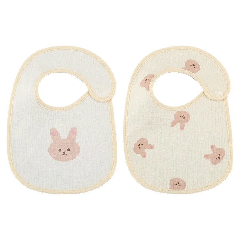 Deux bavoirs bébé de couleur claire avec bordure beige. Celui de gauche a un visage de lapin plus grand, tandis que celui de droite présente plusieurs visages de lapin plus petits. Ces Bavoirs Motifs Bébé 2 Pièces de BABY-PREMA sont aussi élégants que fonctionnels.