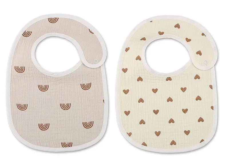 Deux bavoirs bébé sont exposés côte à côte. Le bavoir de gauche, un Bavoirs Motifs Bébé 2 Pièces de BABY-PREMA, présente une couleur beige avec des motifs demi-cercles marron, tandis que le bavoir de droite est de couleur crème avec des motifs cœurs marron. Conçus dans un design Bandana élégant, ces Bavoirs Motifs Bébé 2 Pièces de BABY-PREMA sont à la fois fonctionnels et à la mode.