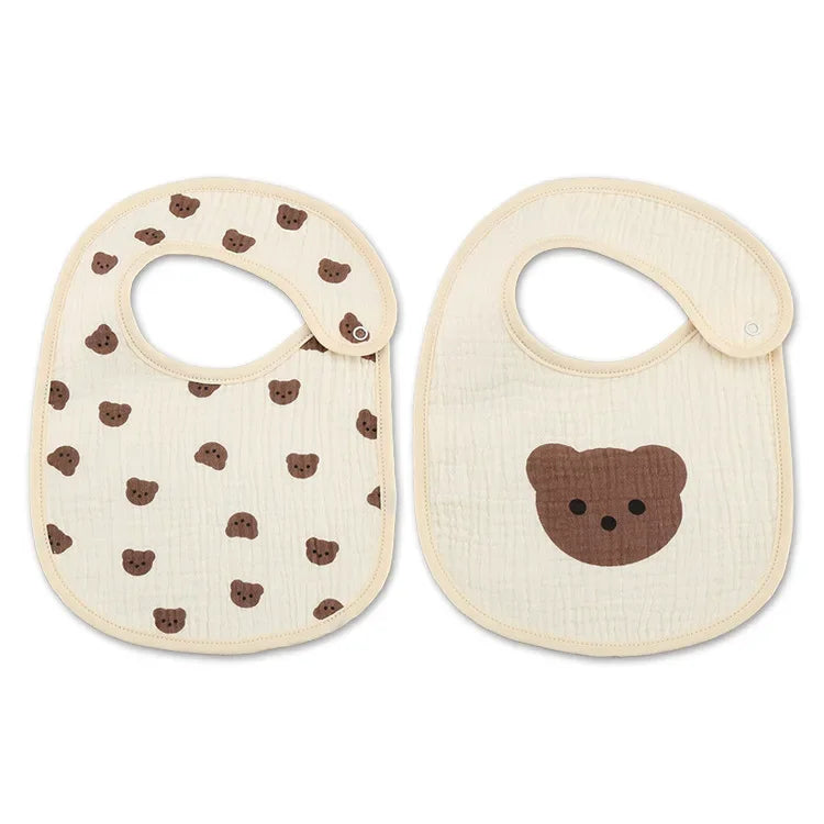 Deux bavoirs pour bébé, chacun avec une fermeture à pression. Le bavoir de gauche présente plusieurs motifs de visages d'ours en peluche, tandis que le bavoir de droite présente un seul grand visage d'ours en peluche au centre. Ces Bavoirs Motifs Bébé 2 Pièces de BABY-PREMA arborent un charmant style Bandana au design parfait pour tout petit.