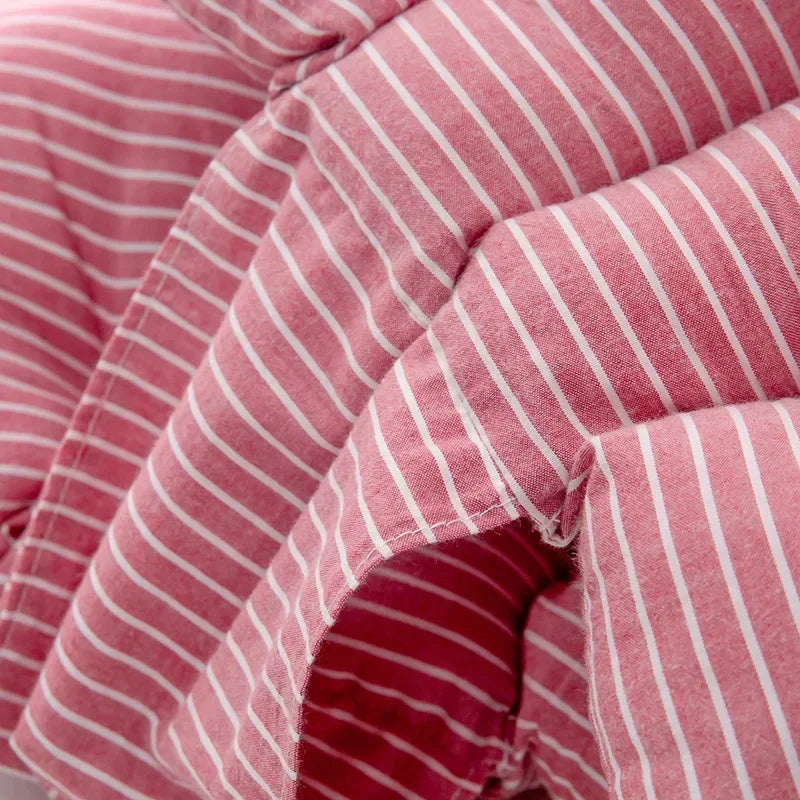 Gros plan d'un tissu rayé rose et blanc, faisant éventuellement partie d'un Oreiller de Grossesse en Coton de BABY PREMA ou d'une couette. Le matériau semble doux et moelleux, avec des coutures et des plis visibles, indiquant qu'il est utilisé pour la literie ou le confort. Les rayures sont verticales et sont uniformément espacées.