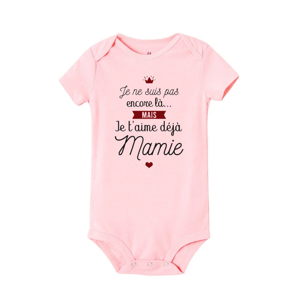 Une combinaison bébé rose, parfaite pour la saison estivale body d'été, comporte un message imprimé en français : « Je ne suis pas encore là... MAIS Je t'aime déjà Mamie », qui se traduit par « Je ne suis pas là ». pourtant... MAIS je t'aime déjà, grand-mère", suivi d'un petit coeur rouge. Le Body Coton été Imprimé de BABY-PREMA est idéal pour ce sentiment.