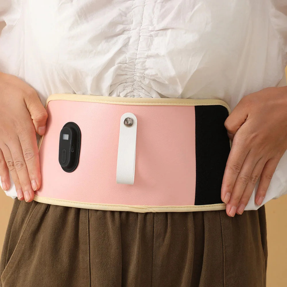 Une personne portant un Chauffe-Biberon Portable multifonction rose de BABY-PREMA sur une chemise blanche et un pantalon marron. La ceinture, portable et multifonction, comporte un petit dispositif de commande noir et une sangle blanche sur le devant. Les mains de la personne sont placées de chaque côté de la ceinture.