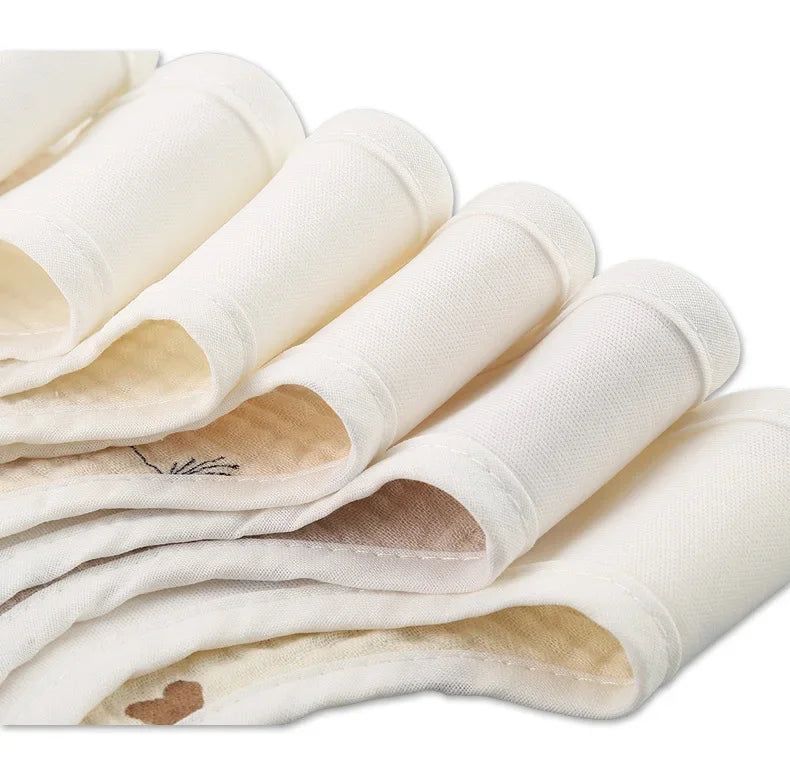 Gros plan de serviettes en tissu blanc soigneusement roulées et disposées en rangée, mettant en valeur leur texture lisse et leur finition épurée, rappelant les Bavoirs Motifs Bébé 2 Pièces avec une touche Bandana au design élégant de BABY-PREMA.