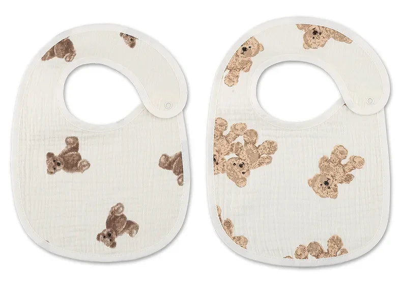 Deux Bavoirs Motifs Bébé 2 Pièces blancs de BABY-PREMA aux imprimés oursons marron. Le bavoir de gauche comporte un seul ours tandis que celui de droite comporte plusieurs ours. Les deux ont des fermetures à pression sur le côté pour plus de commodité.