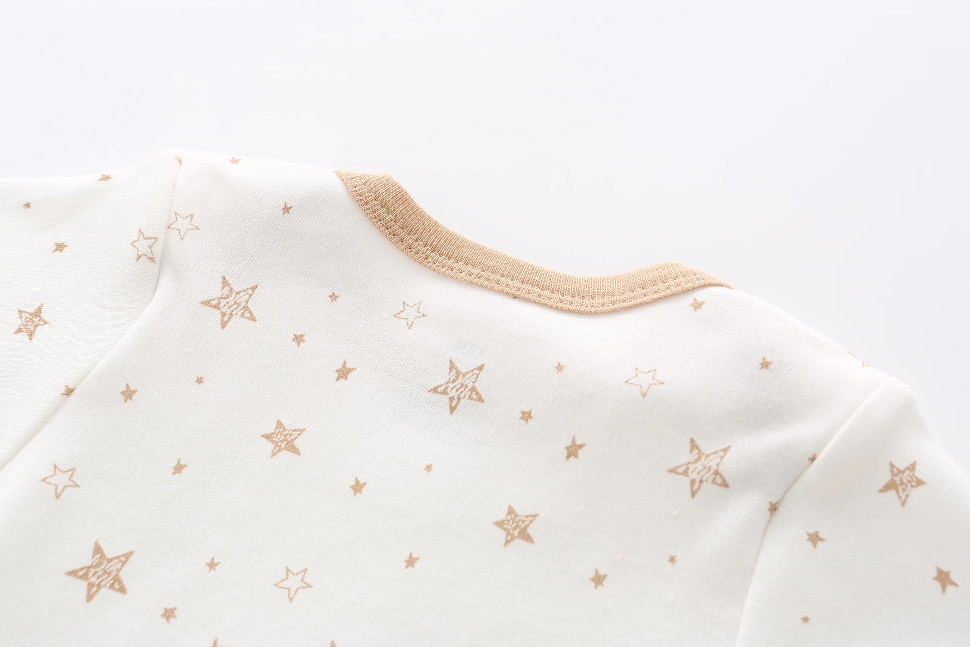 Gros plan sur un vêtement blanc au décolleté beige, orné d'un motif de petites étoiles dorées, parfait pour un trousseau de naissance. Le vêtement fait partie du Lot de 5 Bodys Bébé | Coton Agréables & conforts par BABY PREMA.