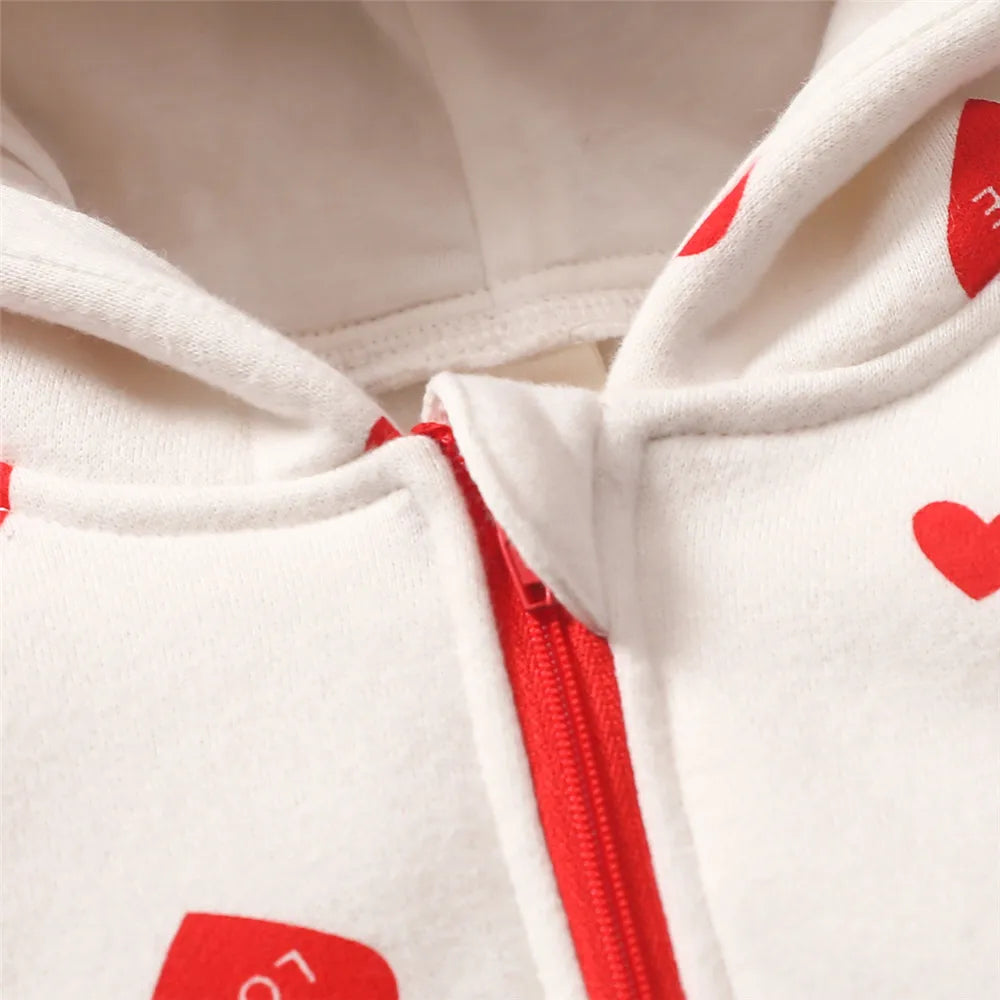 Gros plan d'un sweat à capuche blanc avec une fermeture éclair rouge et des motifs cœurs rouges. Les cœurs portent un petit texte indiquant « AMOUR ». Le tissu semble doux et confortable, suggérant qu'il pourrait s'agir de polaire ou d'un autre matériau chaud, parfait à associer avec la Combinaison pour Nouveau-nés de BABY PREMA pour garder les tout-petits bien au chaud.
