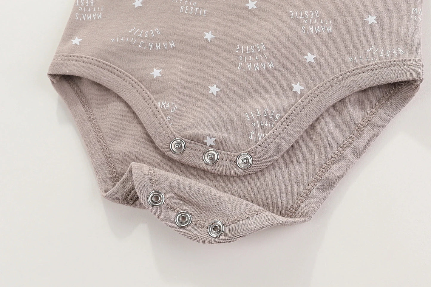 Gros plan sur une combinaison bébé beige, Lot 6 Body Coton Bébé Manches Courtes de BABY PREMA, avec boutons pression et texte blanc et motifs étoiles. Le texte dit : "Mama's Bestie". Cette combinaison bébé à manches courtes se pose à plat.
