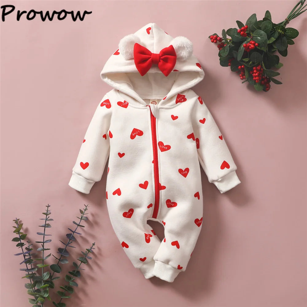 Une combinaison blanche pour bébé avec des cœurs rouges, un nœud rouge et des oreilles blanches moelleuses sur la capuche est présentée sur un fond rose. Le nom de la marque « BABY PREMA » se trouve dans le coin supérieur gauche. Des brins et des baies décoratifs sont placés à côté de cette adorable tenue Combinaison pour Nouveau-nés.