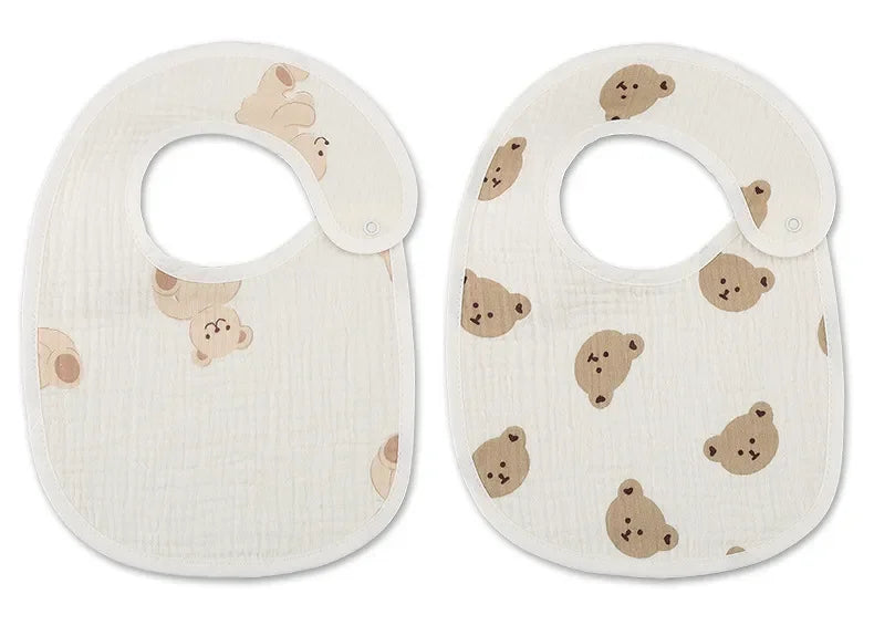 Deux BABY-PREMA Bavoirs Motifs Bébé 2 Pièces blancs à motifs de têtes d'ours. Le bavoir de gauche présente des visages d'ours plus grands et moins nombreux, tandis que le bavoir de droite présente un motif bandana avec des visages d'ours plus petits et plus nombreux. Les deux bavoirs imperméables sont dotés d'une fermeture à pression.