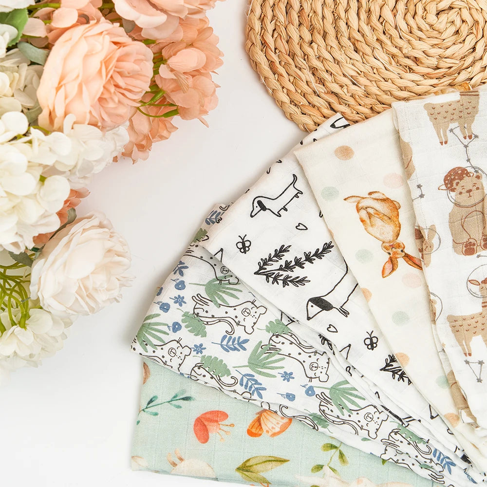 Une composition à plat composée d'un tissu BABY PREMA Langes Lot de 5 pièces Mousseline Coton & Bambou aux illustrations d'animaux, accompagné d'une décoration en osier et d'un bouquet de fleurs artificielles aux couleurs douces, parfait pour créer une ambiance inspirée du dodo.