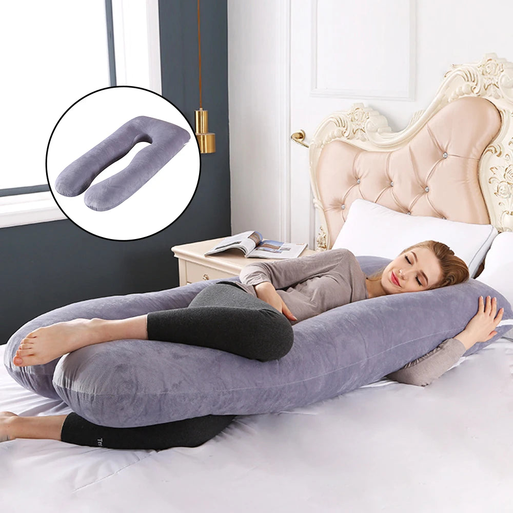 Une femme est allongée sur un lit, se reposant les yeux fermés et serrant dans ses bras un grand Coussin Oreiller Femmes Enceinte gris de BABY PREMA. Elle porte une chemise à manches longues grise et des leggings noirs. L'encart montre un gros plan de l'oreiller en forme de U. Le lit a une tête de lit élégante.