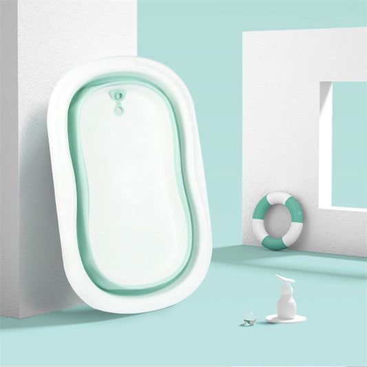 Une salle de bain minimaliste avec une Baignoire pour bébé - Baby Prema blanche autoportante dans un espace au design abstrait, avec une serviette vert pâle et un flacon distributeur blanc pour bain bébé comme accessoires.