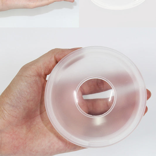 Une main tenant un accessoire Collecteur de lait - Baby Prema transparent en silicone avec un centre creux, sur un fond blanc.