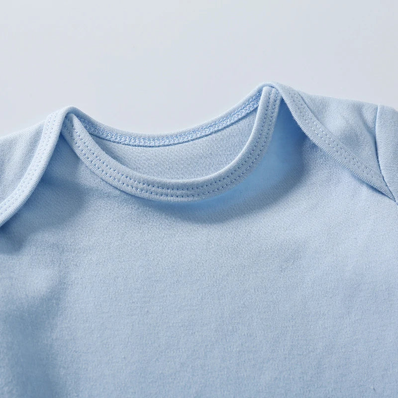 Un gros plan d'un Body Coton Manches Courtes bleu clair fabriqué à partir de tissu en coton doux de BABY-PREMA. L'encolure présente des coutures épurées, ce qui en fait un Body Coton Manches Courtes idéal. La combinaison est étalée à plat sur un fond uni de couleur claire, parfaite comme cadeau pour bébé.