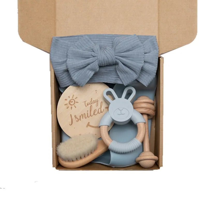 Un ravissant Coffret Cadeau Naissance Bébé de BABY PREMA contenant un bandeau bleu doux avec un nœud, une joyeuse plaque en bois indiquant « Aujourd'hui, j'ai souri », un adorable anneau de dentition en forme de lapin et des produits d'hygiène pour le bain de bébé, y compris un