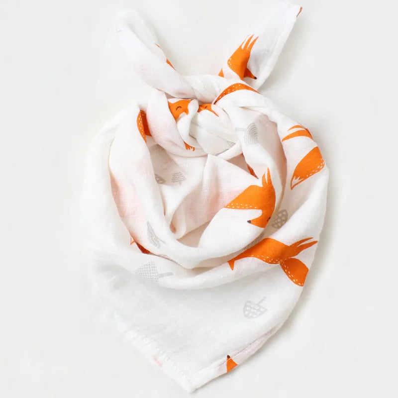 Une écharpe blanche avec un imprimé renard orange ludique, légèrement nouée sur un fond uni, parfaite pour un enfant par Lange Mousseline Coton Bio de BABY PREMA | Emmaillotage de Bébé.