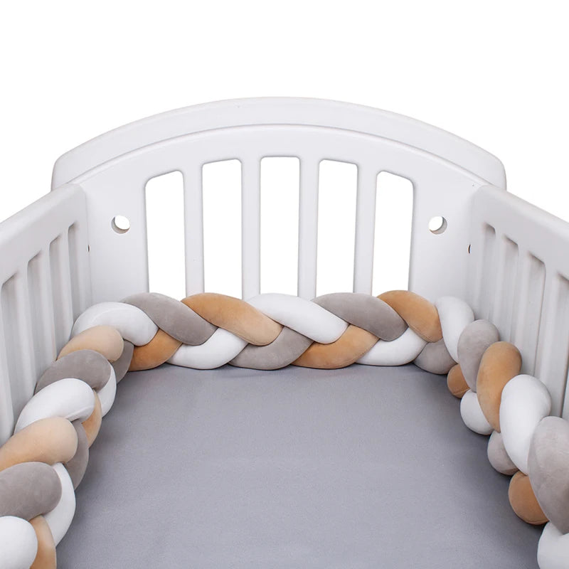 Un berceau blanc avec un matelas gris est présenté avec un élégant tour de lit tressé qui tapisse son intérieur. Le BABY PREMA Tour de Lit Tressé Noué présente des segments entrelacés dans des tons de blanc, de gris et de beige, offrant une barrière protectrice douce et multifonctionnelle.