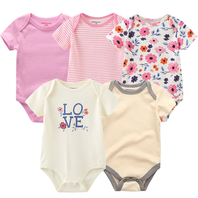 Cinq grenouillères pour bébé de différents modèles et couleurs sont présentées. La collection pour votre garde-robe de bébé comprend une robe rose unie, une à rayures roses et blanches, une à motif floral, une blanche avec le texte "LOVE" et une beige avec bordure grise - un cadeau idéal pour les nouveaux parents. . Présentation du Pack de 5 Bodies | Coton Doux Bébé de BABY PREMA.