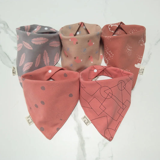 Cinq BABY-PREMA Bavoirs Bandana Coton pour Bébé sont disposés en demi-cercle sur une surface claire. Chaque bavoir présente un design unique : rose avec des feuilles, beige avec des petits motifs colorés, marron avec des formes blanches, rose avec des pois et rouge avec des lignes abstraites. Ces accessoires indispensables pour bébé sont tous dotés de boutons pression.