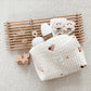 Un ensemble douillet d'essentiels pour bébé avec un Sac de Couches Rangement Bébé de BABY PREMA, des jouets en bois et d'adorables chaussures sur le thème de l'ours en plumes sur un tapis moelleux.