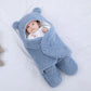 Un bébé douillet enveloppé dans une Couverture Bébé Doux Confortable BABY-PREMA, dans une jolie couverture bleue en forme d'ours avec de petites oreilles, allongé paisiblement sur une surface blanche et douce, entouré d'accessoires bébé.