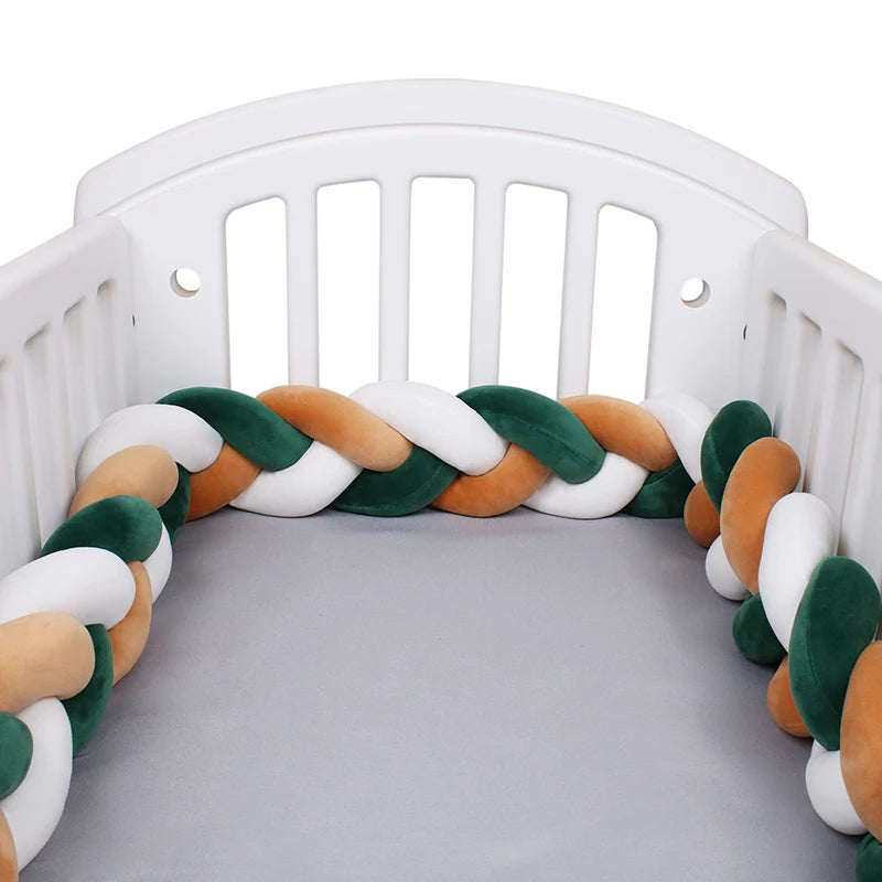 Un lit de bébé avec un Tour de lit bébé 4M tressé de BABY PREMA avec un tour de lit tressé doublé à l'intérieur. Le pare-chocs de lit est composé de brins de peluche entrelacés de couleurs blanc, vert et beige. Le matelas du berceau est recouvert d'un drap gris et le berceau est peint en blanc.