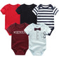 Cinq combinaisons pour bébé sont présentées : un rouge uni, un noir uni, un rayé bleu marine et blanc, un bordeaux avec "#GENIUS" et un bleu clair avec de faux nœuds papillon et des motifs de poche. Ce Pack de 5 Bodies Coton Doux Bébé de BABY PREMA constitue le cadeau de naissance parfait pour tout bébé.