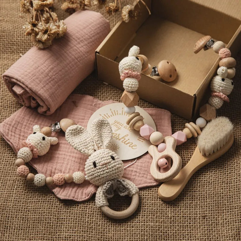 Une collection d'essentiels pour bébé comprenant un Coffret Cadeau Naissance Bébé de BABY PREMA, des jouets en perles de bois et une brosse à cheveux douce soigneusement disposées sur un tissu aux tons neutres, parfaites pour l'hygiène de bébé.