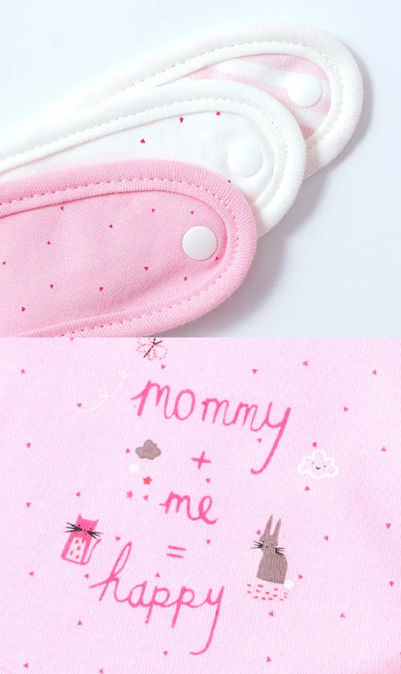 Un gros plan de vêtements pour bébé montre trois boutons-pression blancs et roses en haut. En dessous, il y a un tissu rose avec des petits coeurs et des étoiles. Le texte dit « maman + moi = heureuse » à côté de petits dessins d'un lapin, d'un coffret cadeau, d'un nuage et d'un cœur. Associez-le à l'adorable Lot de 3 pièces Bavoirs Bébé de BABY-PREMA pour plus de charme.