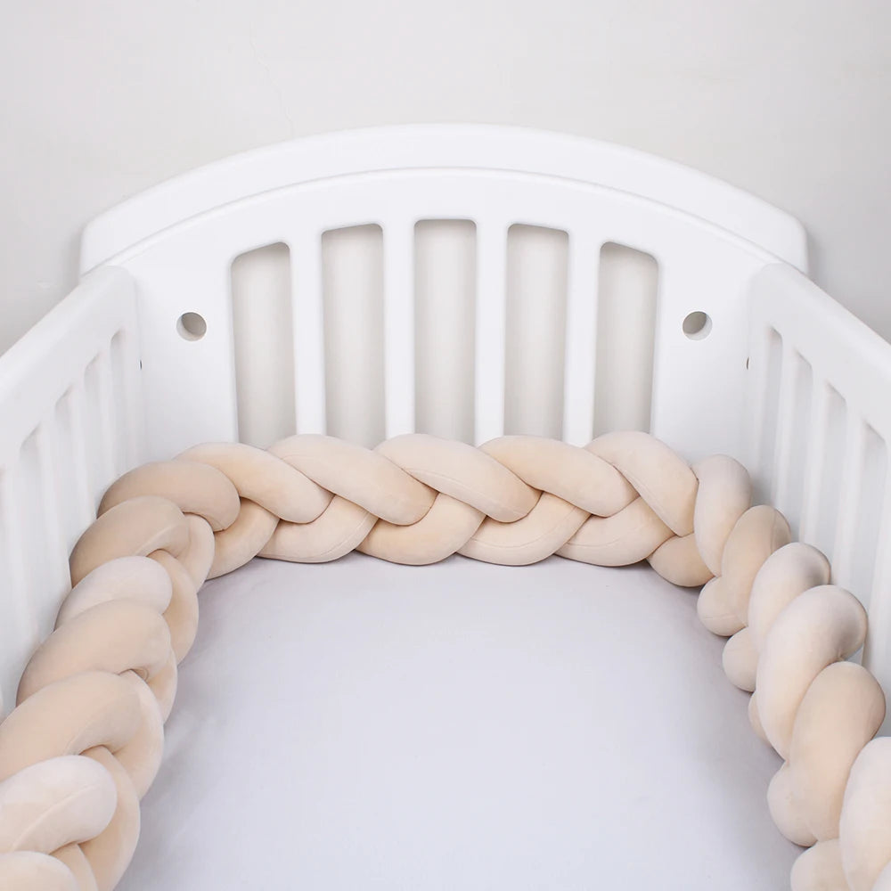 Un berceau blanc à lattes verticales est représenté. À l'intérieur du berceau se trouve un Tour de lit bébé 4M tressé de BABY PREMA dans des couleurs claires et neutres, offrant une doublure protectrice douce autour de l'intérieur. Le mur de fond est uni et blanc.