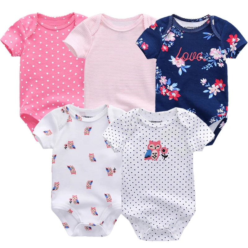 Cinq différents BABY PREMA en coton à manches courtes pour bébés filles présentés, avec des pois, des rayures et des motifs floraux dans des couleurs rose, blanc et bleu marine.