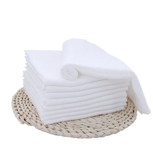 Une pile soignée de serviettes blanches pliées sur un tapis tissé, présentant un aspect propre et organisé, parfait pour les Langes Couvertures & Couches Bébé en Coton de BABY PREMA pendant le temps dodo.
