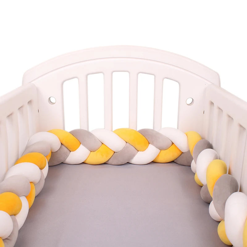 Un lit de bébé blanc avec un matelas gris clair est présenté. Le berceau comporte un Tour de Lit Tressé Noué de BABY PREMA dans des couleurs alternées de jaune, gris et blanc, créant une bordure douce et moelleuse le long de l'intérieur. Ce tour de lit offre une protection supplémentaire du chevet du berceau pour la sécurité et le confort de votre tout-petit.