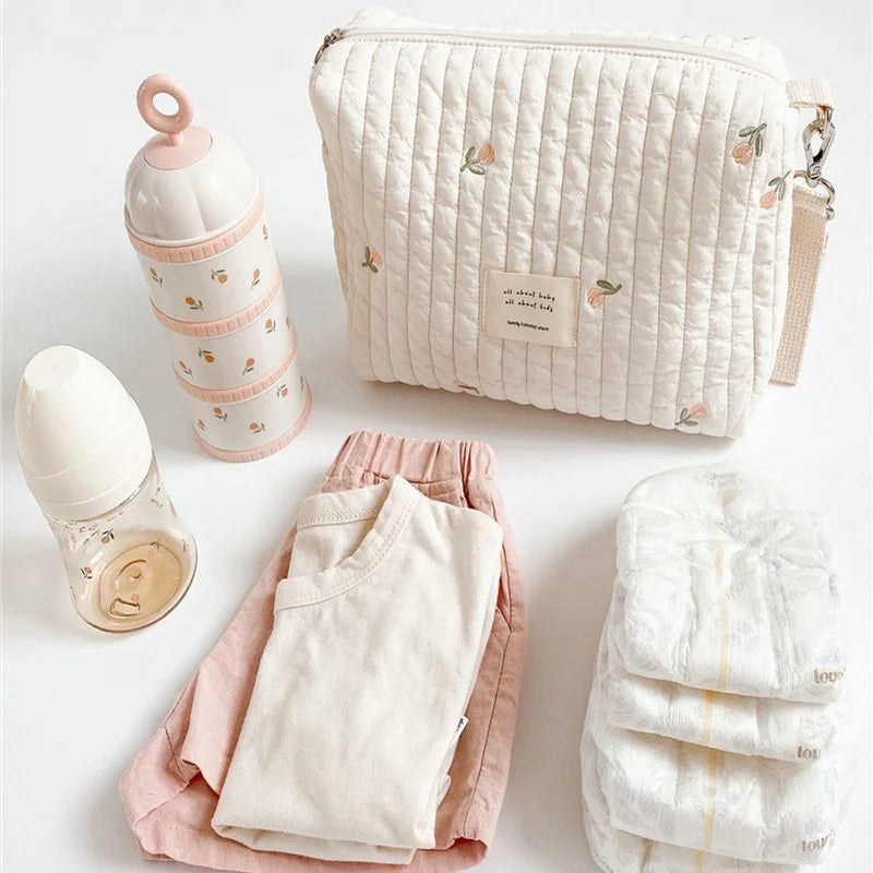 Une collection d'essentiels pour bébé comprenant des vêtements aux couleurs pastel, des couches, un sac Sac de Couches Rangement Bébé et des biberons, soigneusement disposés sur un fond clair pour mon bébé. (Marque : BÉBÉ PREMA)