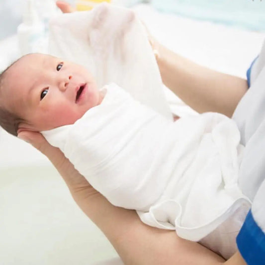 Un nouveau-né BABY PREMA bercé doucement dans des bras aimants, enveloppé dans une Lange Couverture bébé, ouvrant les yeux sur le nouveau monde avec un regard d'émerveillement innocent.