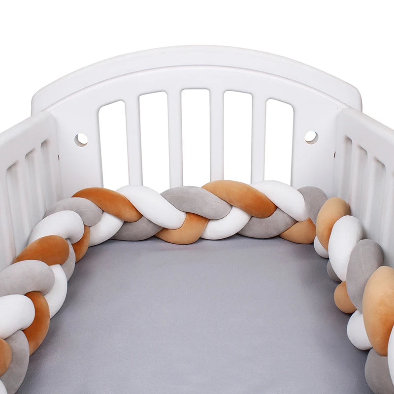 Un lit de bébé blanc avec un BABY PREMA Tour de lit bébé 4M tressé doublé à l'intérieur. Le tour de lit se compose de sections entrelacées de couleurs gris, blanc et beige, créant un environnement doux et confortable pour le bébé. Le matelas du berceau est recouvert d'un drap-housse gris clair.