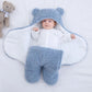 Un bébé bien au chaud, vêtu d'une tenue BABY-PREMA douillette sur le thème de l'ours, doté d'une capuche avec de petites oreilles, allongé sur une couverture douce, l'air curieux et content, entouré d'articles d'hygiène essentiels pour bébé.