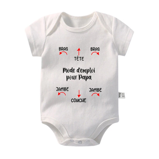 Une combinaison pour bébé en coton blanc avec un texte français noir indiquant « Mode d'emploi pour Papa », avec des flèches pointant vers des parties étiquetées comme « BRAS » (bras) et « TÊTE » (tête). Cet adorable Body Coton Imprimé de BABY-PREMA assure que votre bébé reste confortable pendant les journées chaudes tout en étant facile à habiller.