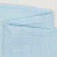 Un gros plan d'un tissu texturé bleu clair avec une Lange Couverture bébé | Emmaillotage Mousseline Bambou au tissage lâche et aux bords légèrement effilochés par BABY PREMA.