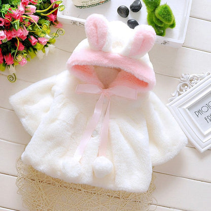 Un manteau gilet pour bébé douillet et adorable de BABY PREMA avec des oreilles de lapin roses et un ruban à nouer, affiché sur une surface plane avec des fleurs décoratives et des cailloux autour, parfait pour votre poids léger.