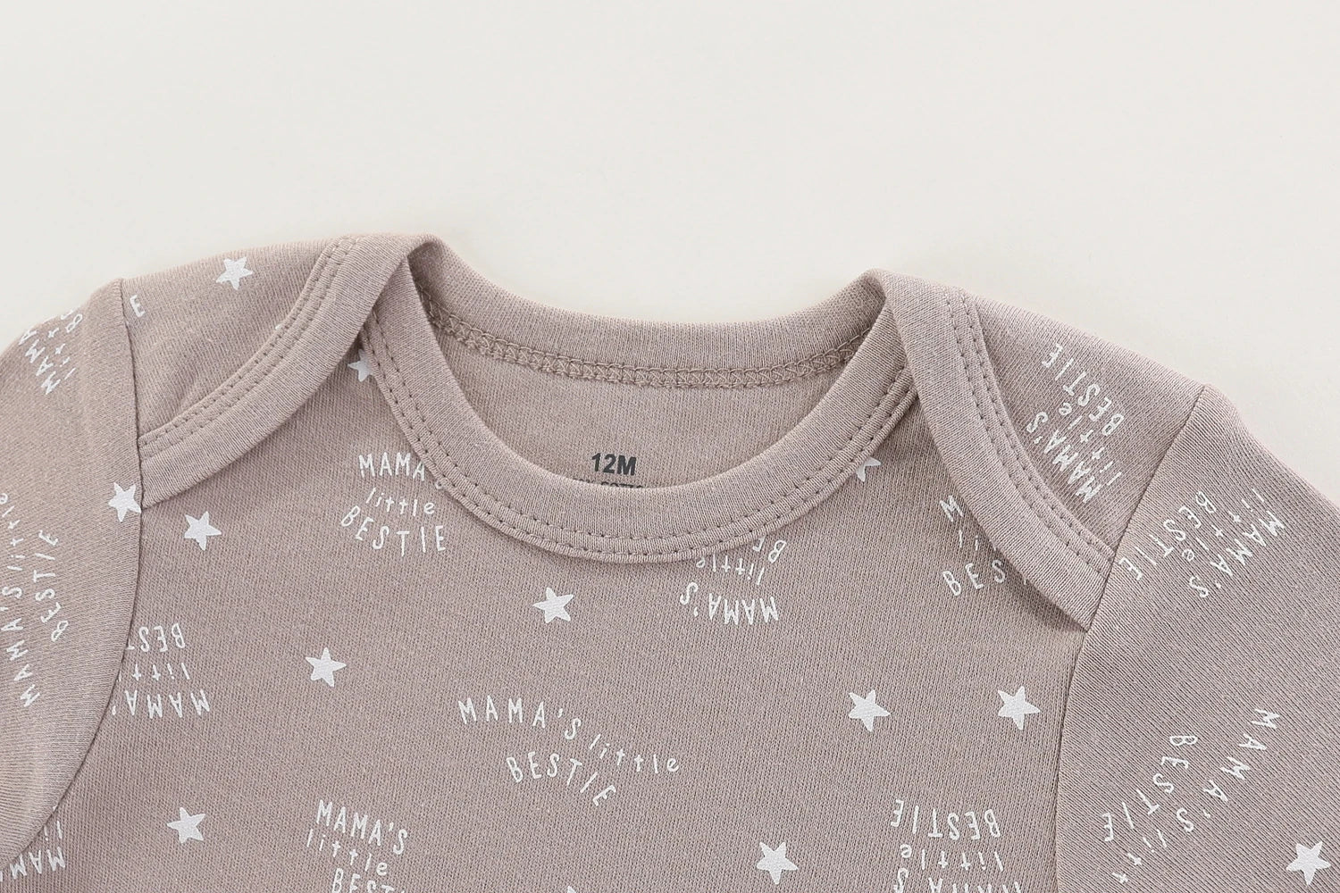 Gros plan sur un Lot 6 Body Coton Bébé Manches Courtes gris à manches courtes de BABY PREMA, en coton doux avec un motif étoilé et le texte "Mama's Little Bestie" imprimé à plusieurs reprises. Parfait comme cadeau de naissance, la taille imprimée sur le décolleté est 12M.