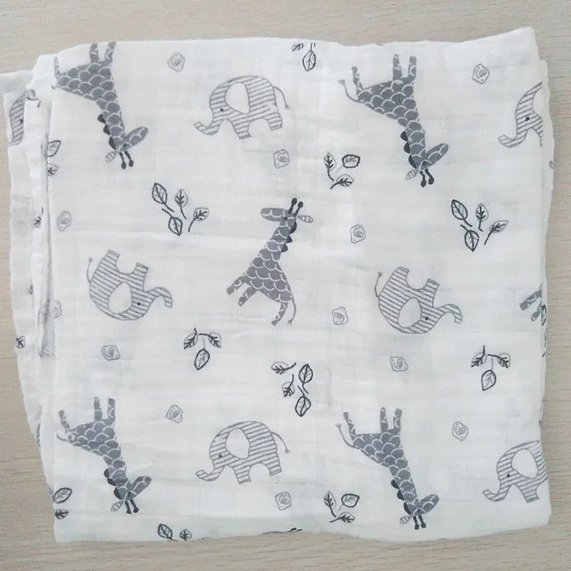 Un article bébé : une Couverture en Mousseline de Coton pour Bébé BABY PREMA avec un motif ludique d'éléphants et de girafes, entremêlés de motifs feuilles.