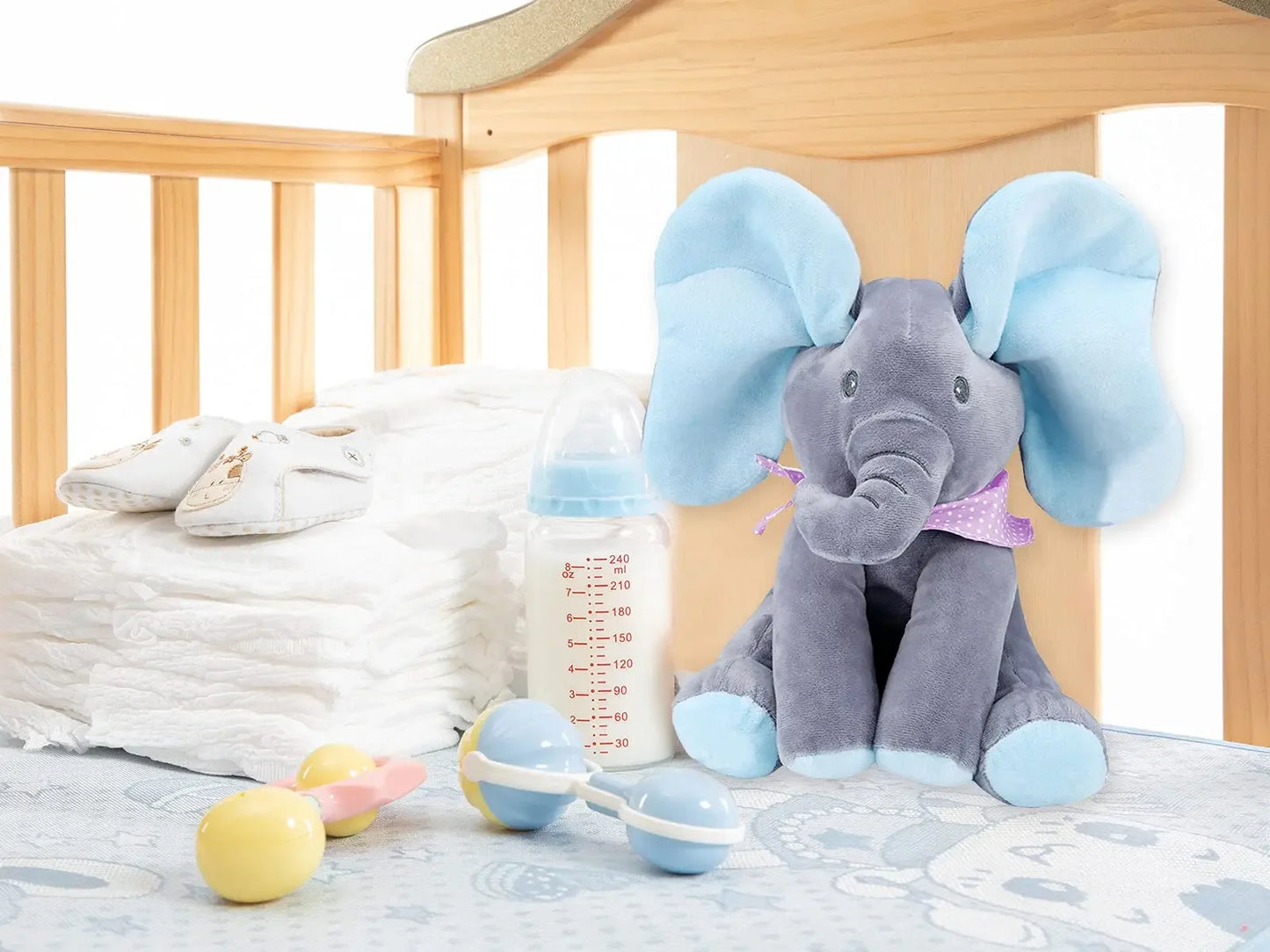 Un Doudou Éléphant Musicale BABY-PREMA assis sur le lit d'un bébé prématuré, avec un biberon, une paire de petites chaussures blanches et deux maracas jouets à proximité, créant une chambre de bébé chaleureuse et nourrissante.