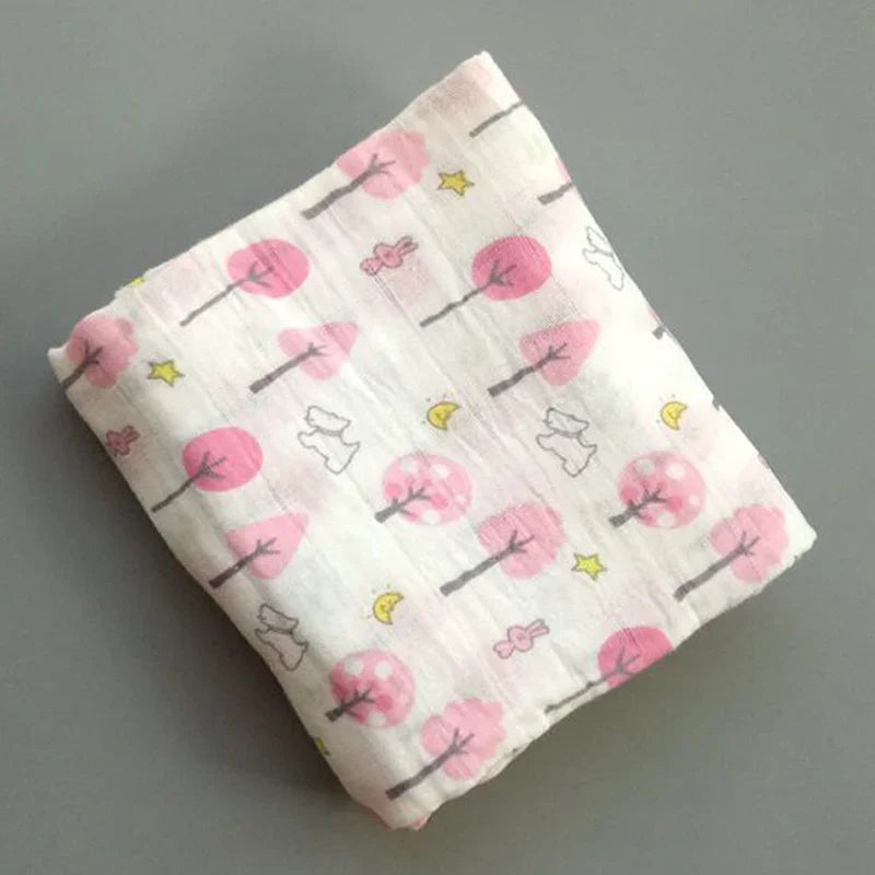 Une Couverture en Mousseline de Coton pour Bébé de la marque BABY PREMA présentant un schéma de couleurs rose et blanc, ainsi qu'un motif d'arbres, d'oiseaux et d'étoiles.