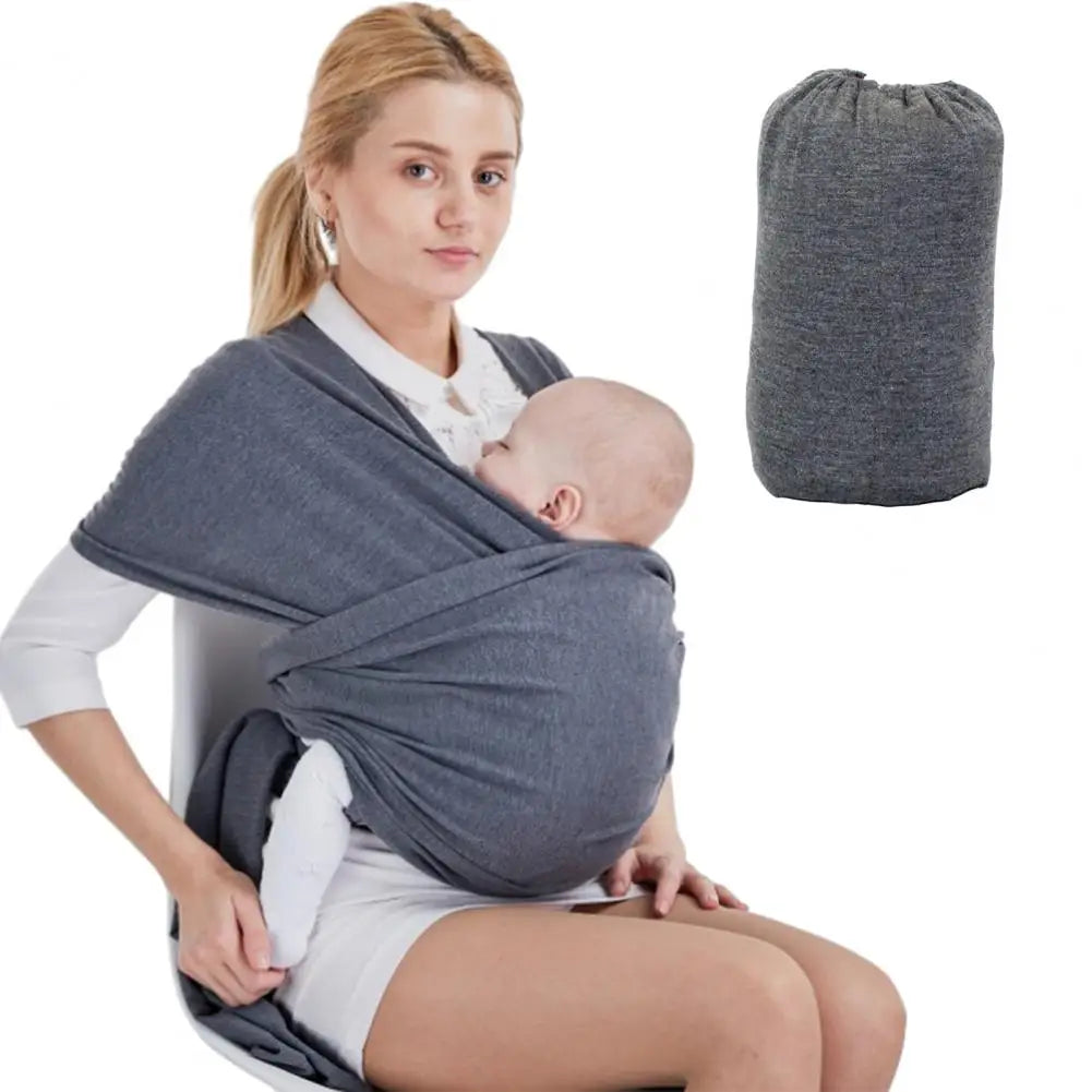 Une femme, les cheveux tirés en arrière, est assise pendant qu'elle allaite un bébé dans une « BABY-PREMA Porte-Bébé dès la Naissance | Echarpe de Portage » gris foncé, avec une image de l'écharpe pliée à côté d'elle.
